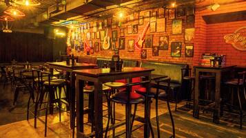 A bar area with multiple stools and tables, a brick wall with framed pictures, and a neon sign.
