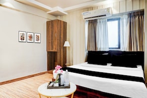 Habitación de hotel con cama, mesita de noche con bandeja, aire acondicionado de pared y ventana con cortinas.