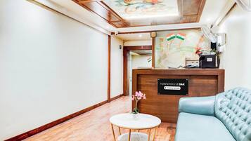 A reception area with a wooden reception desk, a small round table with a vase, and a blue sofa.