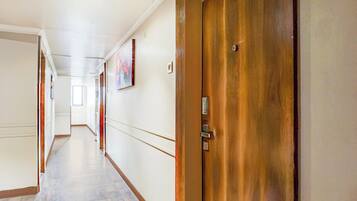 A hallway with a wooden door, white walls, and a painting on the wall.