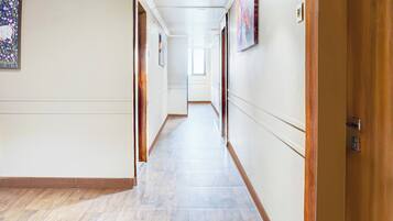 A long, narrow hallway with a wooden floor and white walls, leading to a door at the end.