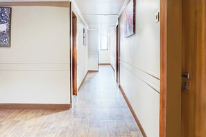 Un largo y estrecho pasillo con suelo de madera y paredes blancas, que conduce a una puerta al final.