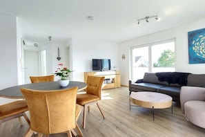 A modern living room with a sofa, a coffee table, and a dining area with chairs and a table. - Holiday apartment with 2 bedrooms (Lindau)