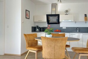 A modern kitchen with white cabinets, a black range hood, and a dining area with a round table and four chairs. - Holiday apartment with 2 bedrooms (Lindau)