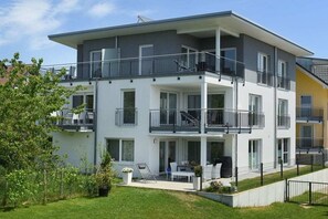 Un edificio residencial de varios pisos con balcones, una zona de estar al aire libre techada y un césped bien cuidado.
