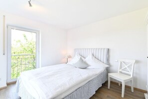 A bedroom with a bed, a chair, a nightstand, and a window with a view of greenery. - Holiday apartment with 2 bedrooms (Lindau)