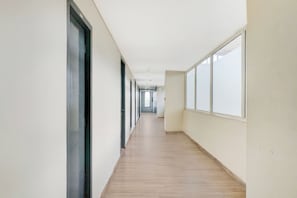 Un pasillo largo y estrecho con piso de madera y ventanas grandes a un lado.
