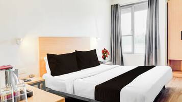 A hotel room with a bed, bedside table, lamp, and a window with curtains.