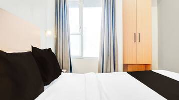 A hotel room with a bed, a wardrobe, and a window with curtains.