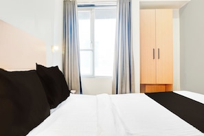 Una habitación de hotel con una cama, un armario y una ventana con cortinas.
