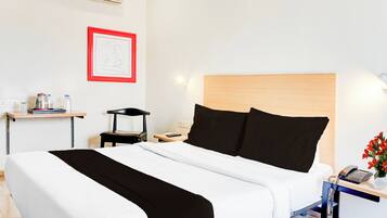 A hotel room with a bed, bedside table, chair, and a wall-mounted air conditioner.