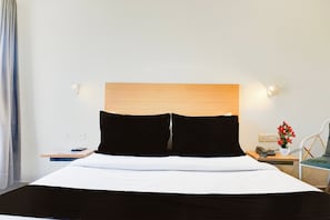 Habitación de hotel con cama, mesita de noche, lámpara, teléfono y un florero con flores.