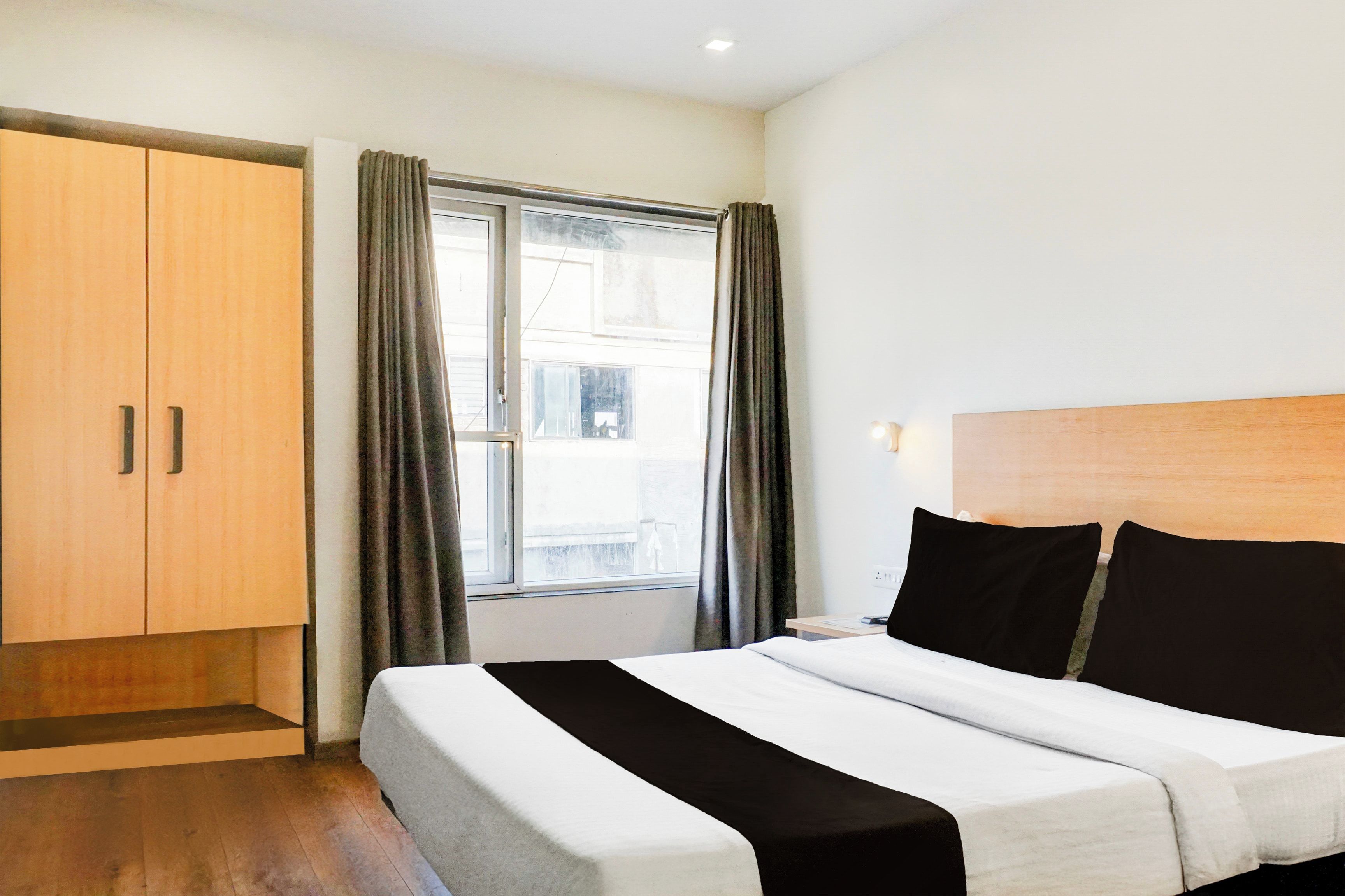 A hotel room with a bed, a wardrobe, a window with curtains, and a view of the outside.