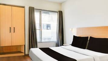 A hotel room with a bed, a wardrobe, a window with curtains, and a view of the outside.