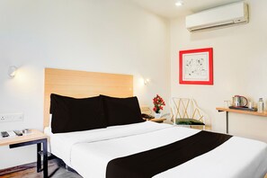 Habitación de hotel con cama, mesita de noche, lámpara, silla y aire acondicionado instalado en la pared.