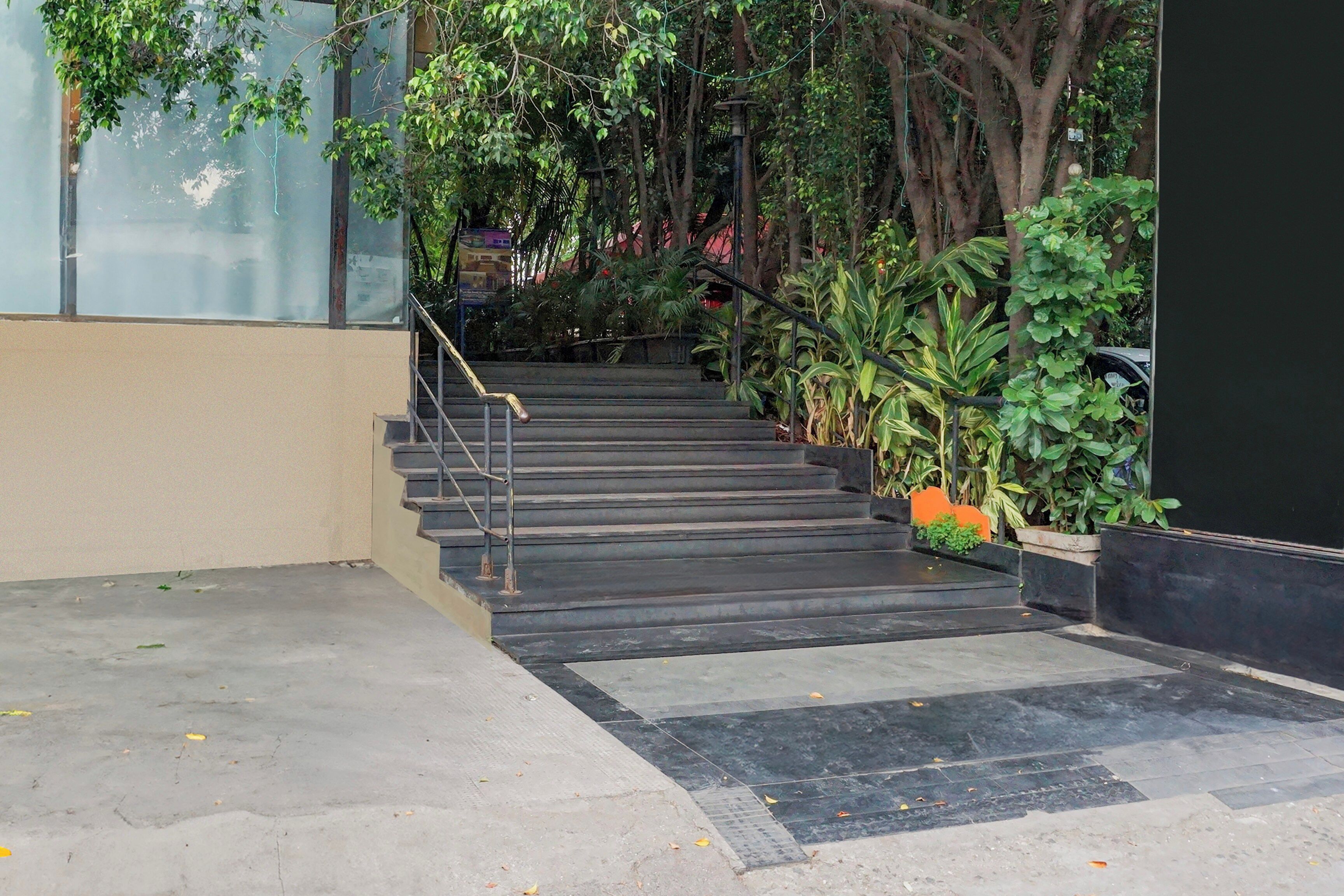Una escalera conduce a la entrada de un edificio, rodeada de vegetación y una pared de vidrio.