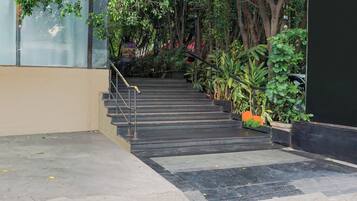 Una escalera conduce a la entrada de un edificio, rodeada de vegetación y una pared de vidrio.
