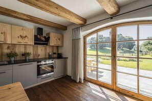 Une cuisine avec des meubles de rangement en bois, un four encastré et une grande fenêtre donnant sur un jardin.