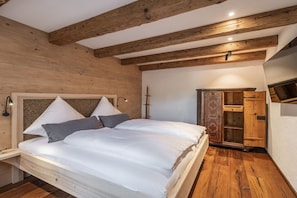 A bedroom with a wooden ceiling, a bed with white bedding, a nightstand, and a wardrobe. - Home - Apartment Liesl (Surberg)