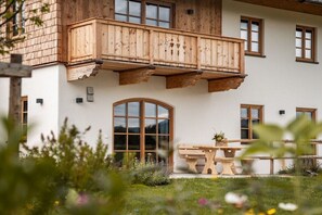 A two-story building with a wooden balcony, a large arched window, and a table with a plant in the foreground. - Home - Apartment Liesl (Surberg)