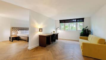 Una habitación moderna con piso de espiga, una cama con cabecera capitonada, un escritorio con lámpara y un sofá amarillo.