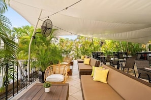 An outdoor seating area with wicker furniture, a sofa, and a fan under a canopy. - Parasasa Hotel Curacao (Willemstad)