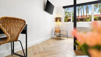 Una habitación moderna con suelo tipo espiga, un televisor de pantalla plana en la pared y una ventana con vista a palmeras.