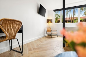 A modern room with a herringbone floor, a flat-screen TV mounted on the wall, and a window with a view of palm trees. - Parasasa Hotel Curacao (Willemstad)