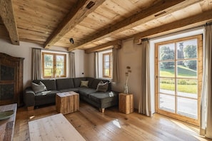 A cozy living room with a wooden ceiling, a sectional sofa, and a large window with a view of greenery. - Home - Apartment Ludwig (Surberg)
