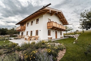 A two-story chalet with wooden balconies, a stone foundation, and a garden with benches. - Home - Apartment Ludwig (Surberg)