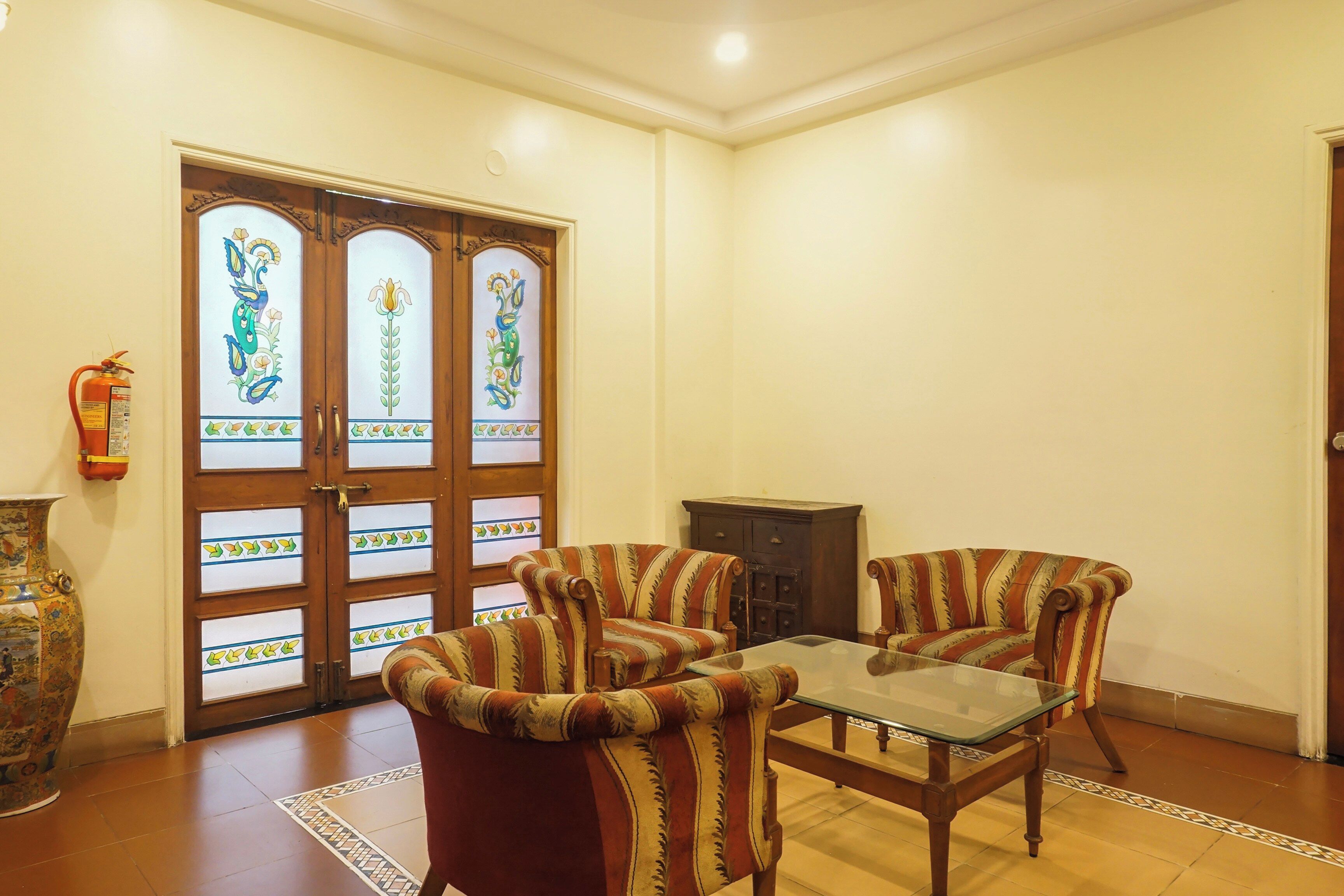 A room with a glass-top table, two striped armchairs, a wooden cabinet, and a decorative door with floral designs.