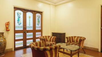 A room with a glass-top table, two striped armchairs, a wooden cabinet, and a decorative door with floral designs.