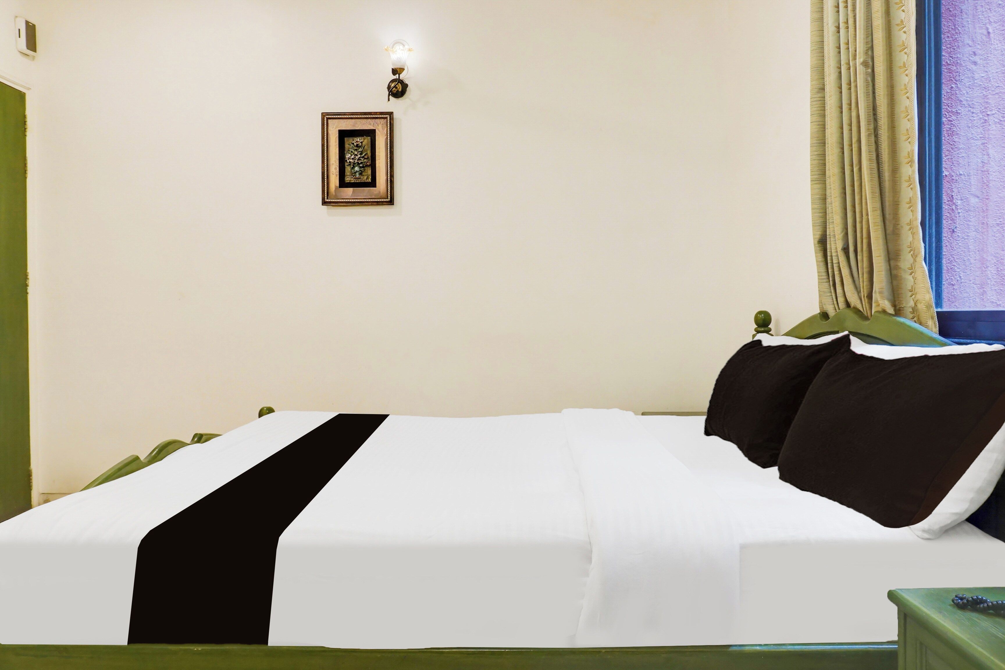 A hotel room with a bed, a nightstand, a wall-mounted lamp, and a framed picture.