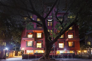 A multi-story building with illuminated windows and a tree in front. - Townhouse Oak Prabhat Road (Pune)