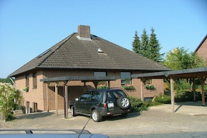 A brick building with a covered parking area and a car parked in front. - Holiday apartment with 1 bedroom (Bispingen)