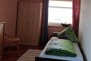A bedroom with a bed, a wardrobe, a chair, and a window with curtains. - Holiday apartment with 1 bedroom (Bispingen)