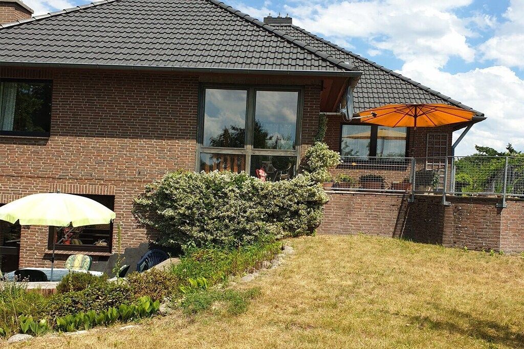 A brick house with a tiled roof, a patio with a yellow umbrella, and a small garden area.