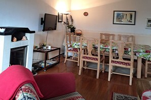 A living room with a fireplace, a television mounted on the wall, a dining table with chairs, and a red sofa. - Holiday apartment with 1 bedroom (Bispingen)