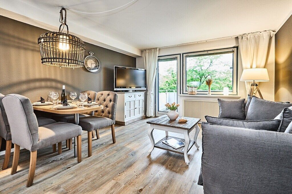 A modern living room with a dining area, a sofa, a TV, and a window with a view of greenery.