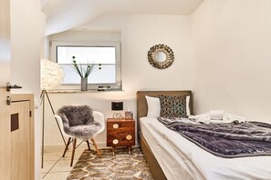 Un dormitorio con cama, una silla, mesita de noche, lámpara y ventana con vistas.