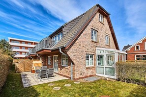 A two-story brick house with a sloped roof, a balcony, and a glass door leading to a covered patio area. - Holiday apartment with 3 bedrooms (Westerland)