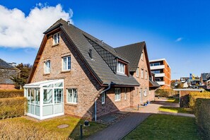 A two-story house with a sloped roof, a conservatory, and a paved driveway. - Holiday apartment with 3 bedrooms (Westerland)
