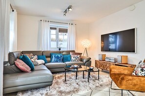 A modern living room with a sectional sofa, a coffee table, and a flat-screen TV mounted on the wall. - Holiday apartment with 2 bedrooms (Westerland)