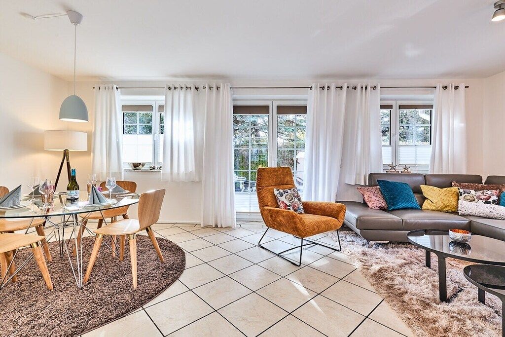 A modern living room with a glass dining table, a sofa, a brown armchair, and a coffee table.