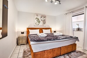 A bedroom with a large bed, a headboard, a nightstand, a wall-mounted artwork, and a window with curtains. - Holiday apartment with 2 bedrooms (Westerland)