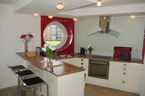A modern kitchen with a central island, stainless steel appliances, and a red accent wall. - Strandpalais, Apt. 508 (Cuxhaven)