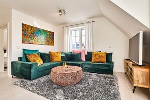 A modern living room with a sectional sofa, a round coffee table, and a television on a wooden cabinet. - Holiday apartment with 3 bedrooms (Westerland)