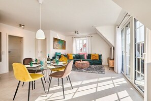 A modern living room with a dining area, large windows, and a view of the outside. - Holiday apartment with 3 bedrooms (Westerland)