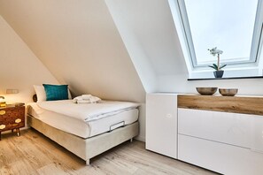 A modern bedroom with a bed, a nightstand, a window with a view, and a plant on the windowsill. - Holiday apartment with 3 bedrooms (Westerland)