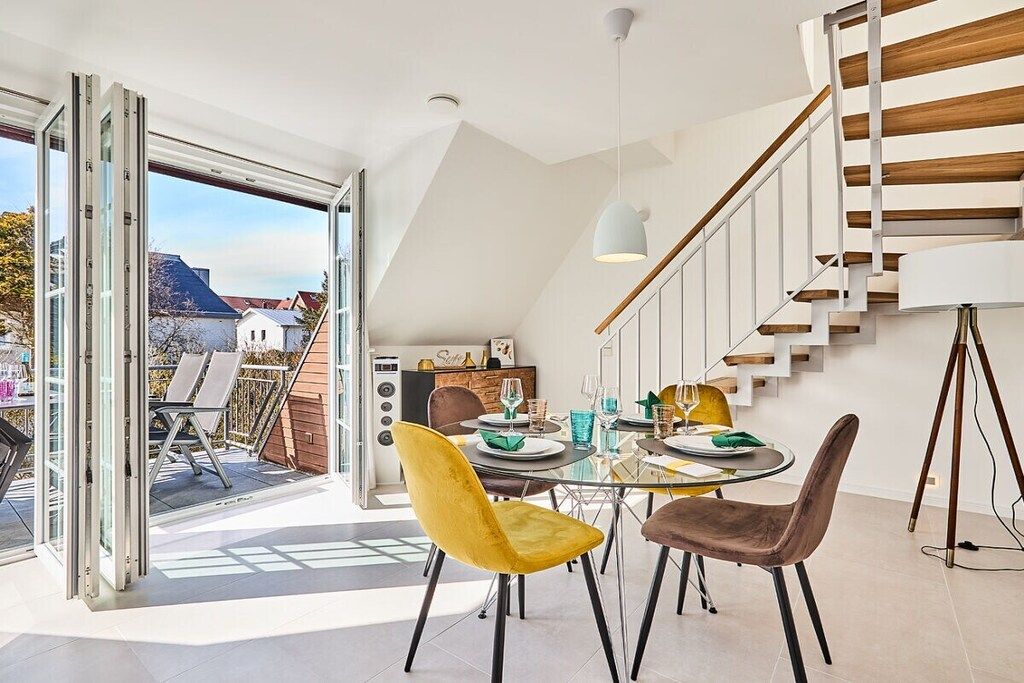 A dining area with a glass table, two chairs, and a modern staircase.